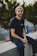 man in black crew neck t-shirt and blue denim jeans sitting on gray concrete bench