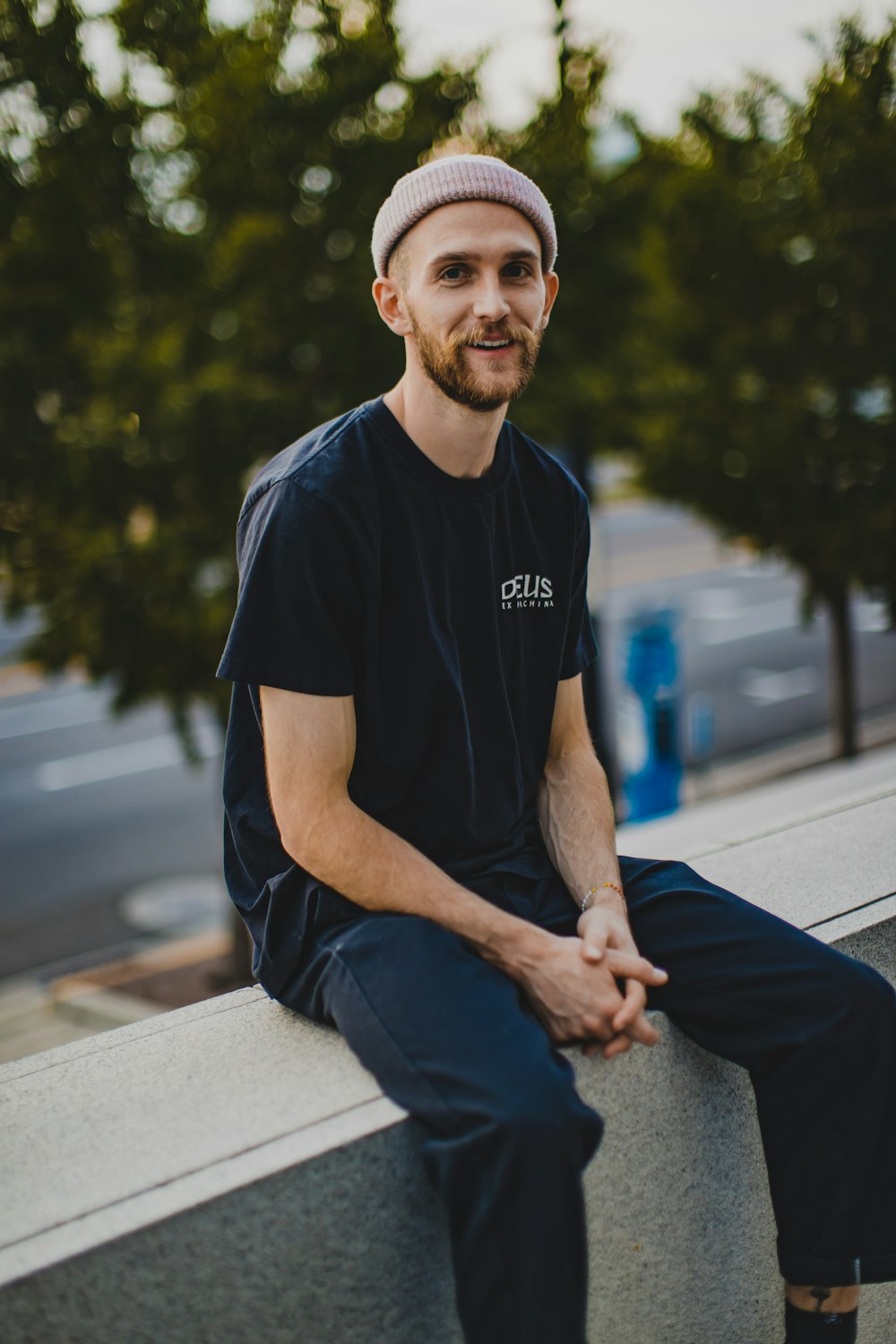 man in black crew neck t-shirt and blue denim jeans sitting on gray concrete bench