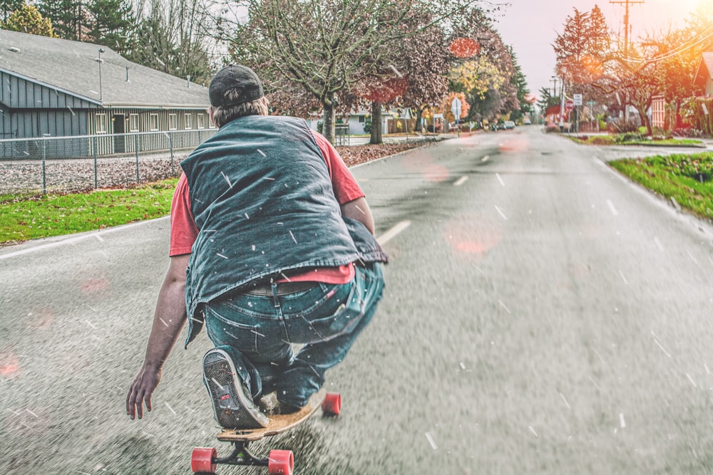 man in blue denim jeans riding on black skateboard on gray asphalt road during daytime