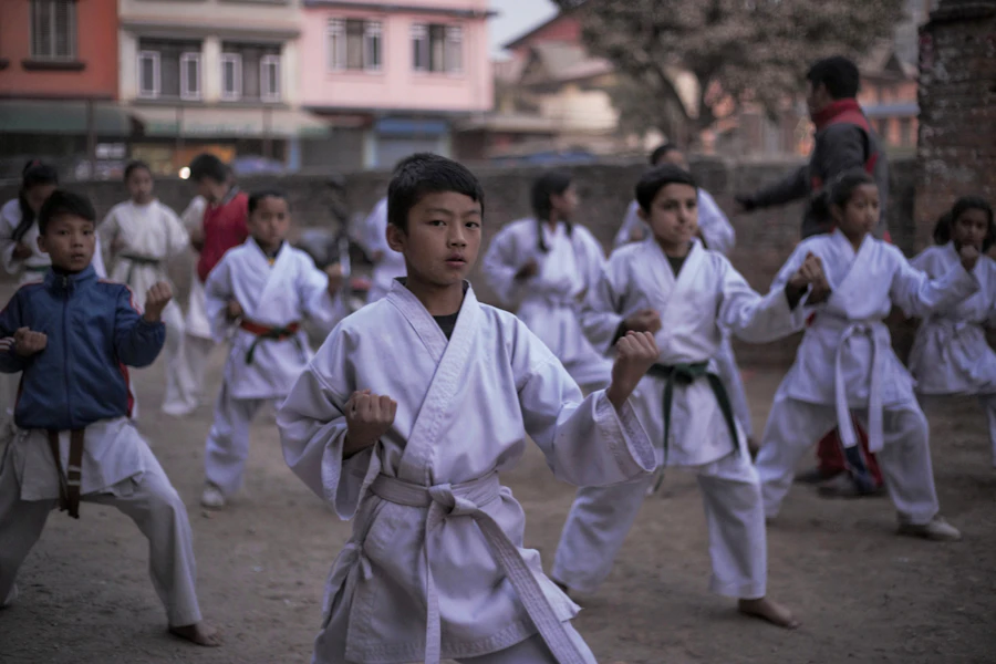 Children in white uniforms training outdoors with staffs