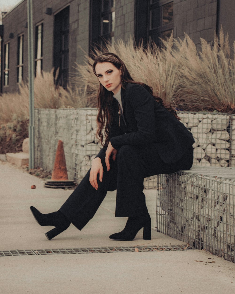 woman in black coat and black pants sitting on concrete wall during daytime