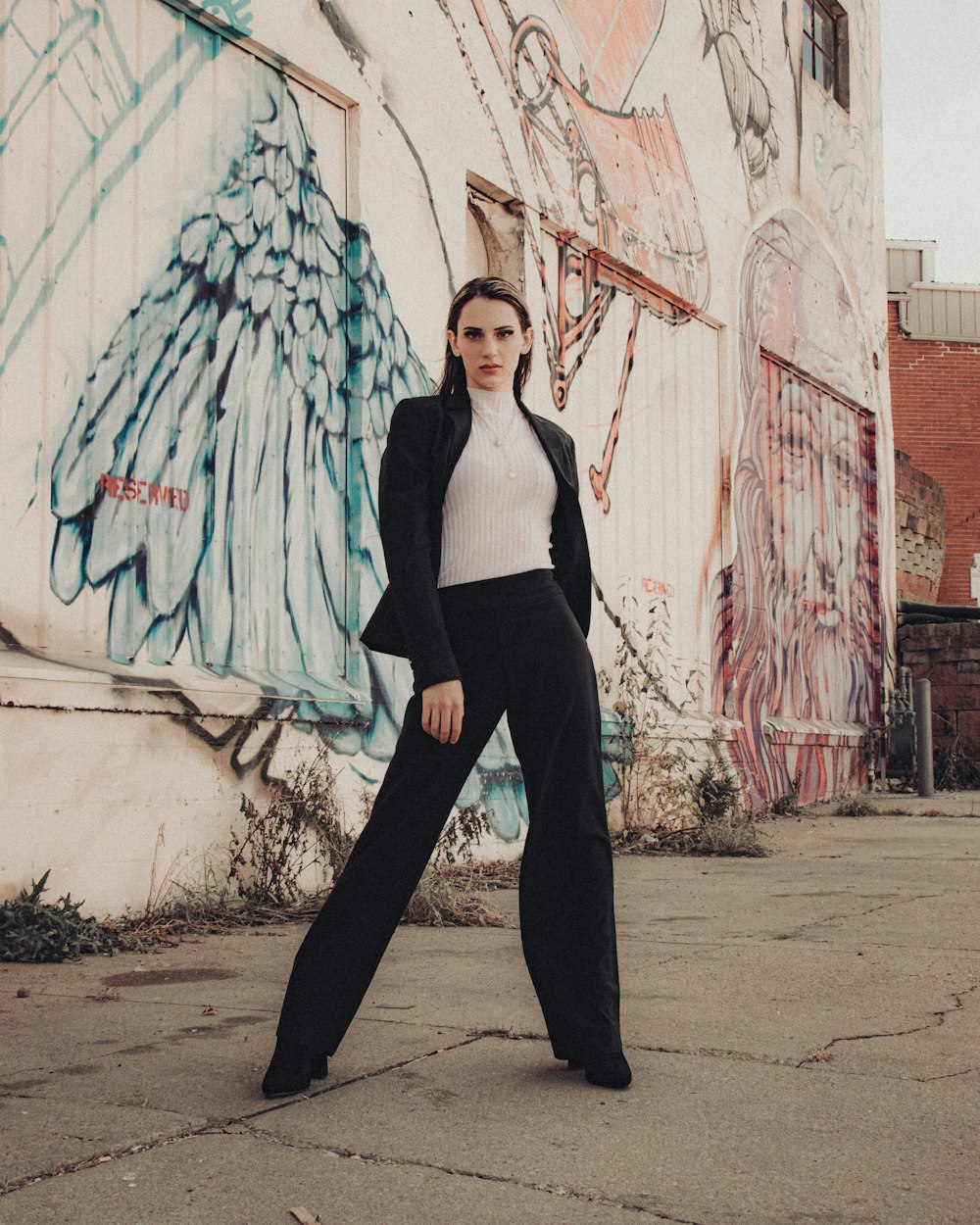 woman in black tank top and black pants standing beside wall with graffiti during daytime