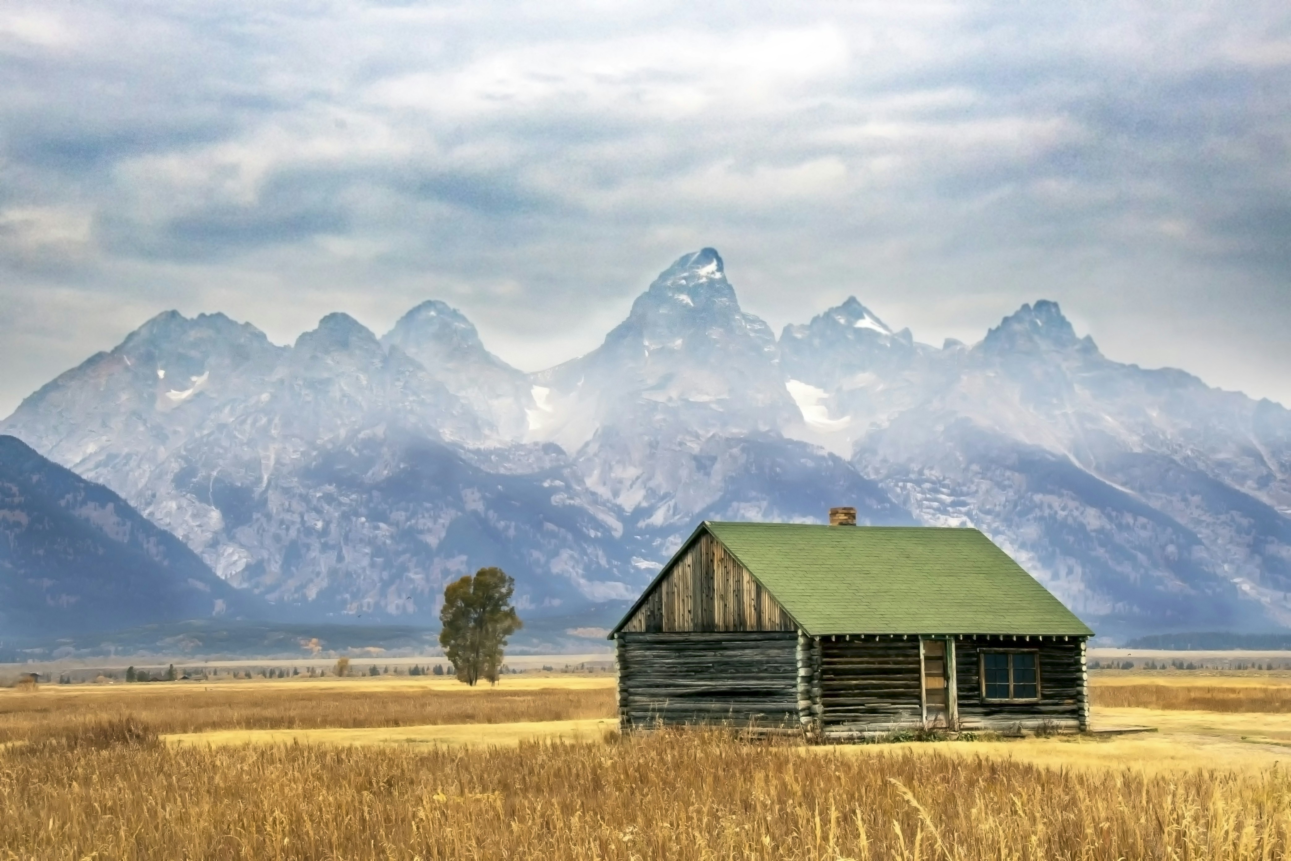brown wooden house on brown grass field near mountains under white clouds during daytime