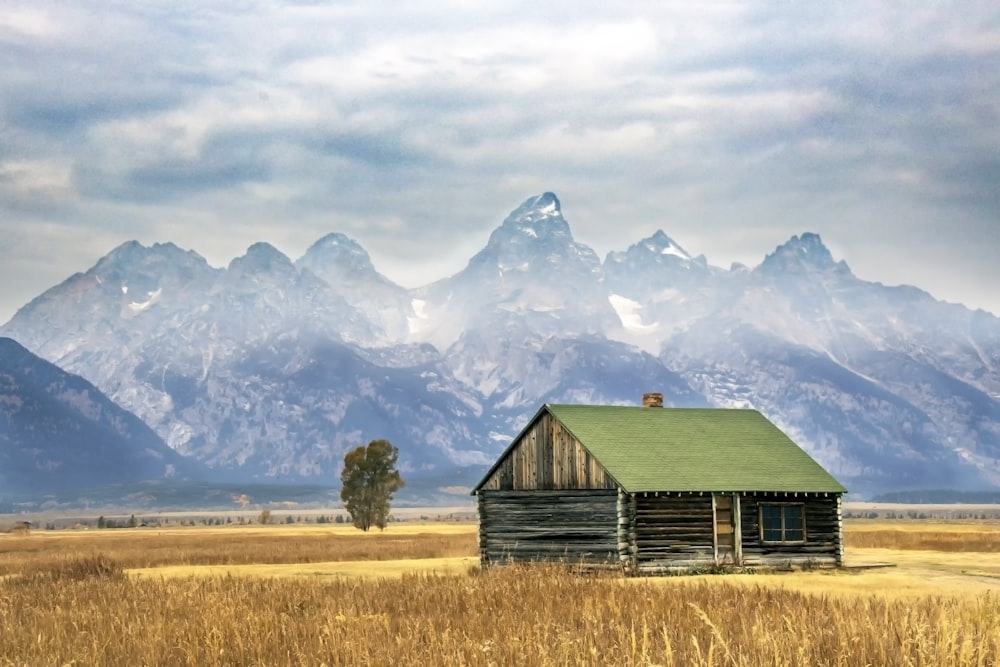 Maison en bois marron sur un champ d’herbe brune près des montagnes sous les nuages blancs pendant la journée