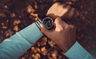 Close-up of a man adjusting his watch, wearing a soft grey cardigan over a light blue shirt.