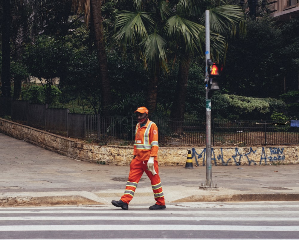 man in orange jacket and pants walking on sidewalk during daytime