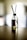 A glass diffuser bottle with a silver top and black reed sticks is placed on a wooden surface. The background is softly blurred, creating a serene atmosphere.
