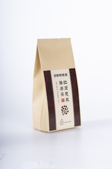 A beige paper package with vertical brown panels on either side, featuring text in Chinese and English. The front includes an illustration of scattered beans and specific details indicating a type of tea.