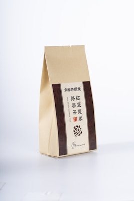 A beige paper package with vertical brown panels on either side, featuring text in Chinese and English. The front includes an illustration of scattered beans and specific details indicating a type of tea.