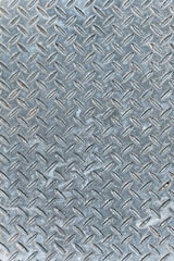 An industrial metal surface with a raised diamond plate pattern, often used for traction and durability. The surface appears weathered with slight discoloration and scuff marks.