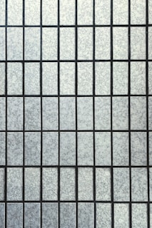 A grid pattern composed of rectangular frosted glass panes with a textured surface. The panes are uniformly arranged and separated by thin, dark lines creating a symmetrical appearance.
