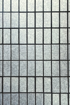 A grid pattern composed of rectangular frosted glass panes with a textured surface. The panes are uniformly arranged and separated by thin, dark lines creating a symmetrical appearance.