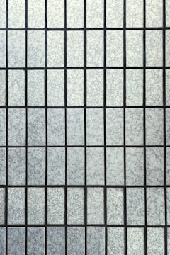 A grid pattern composed of rectangular frosted glass panes with a textured surface. The panes are uniformly arranged and separated by thin, dark lines creating a symmetrical appearance.
