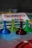 Four translucent game pieces in blue, yellow, red, and green are arranged on a board with a blurred background featuring game cards and other elements.