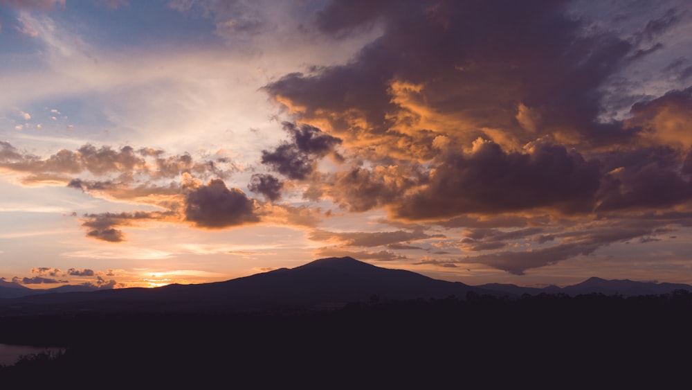 silhouette of mountain under cloudy sky during sunset