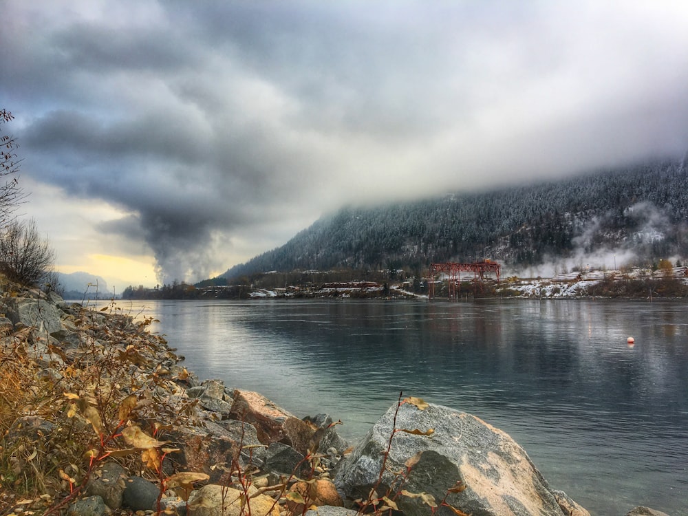 body of water near mountain under cloudy sky during daytime