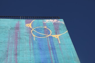 An artist painting a large abstract mural on a bright wall outdoors.