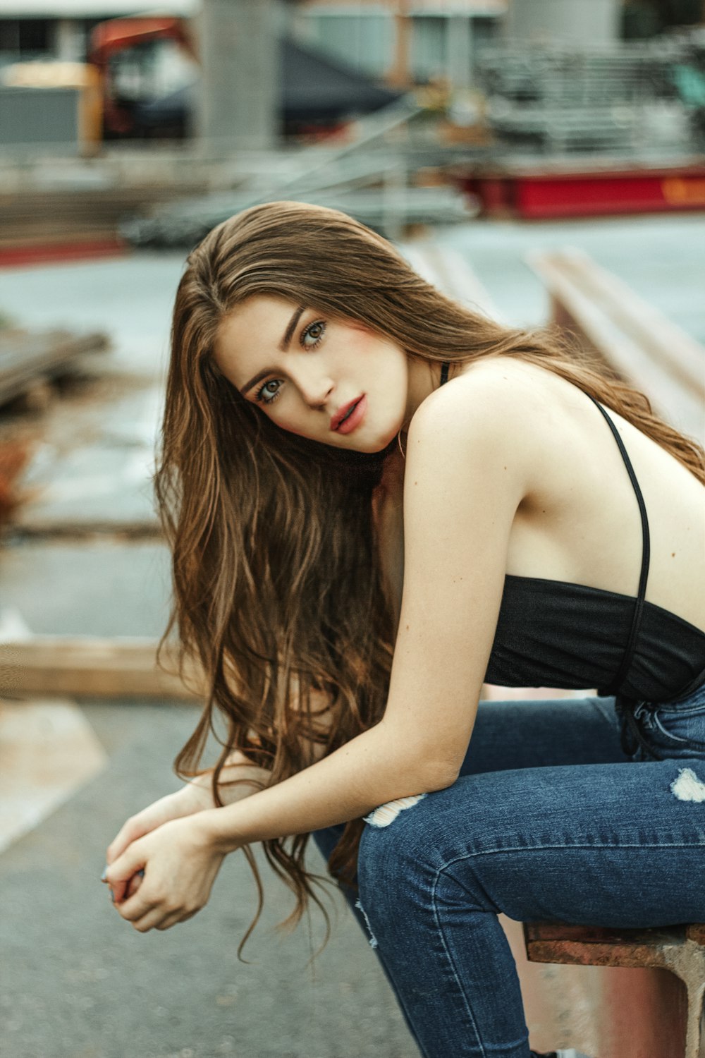 woman in black spaghetti strap top and blue denim jeans sitting on brown wooden bench during
