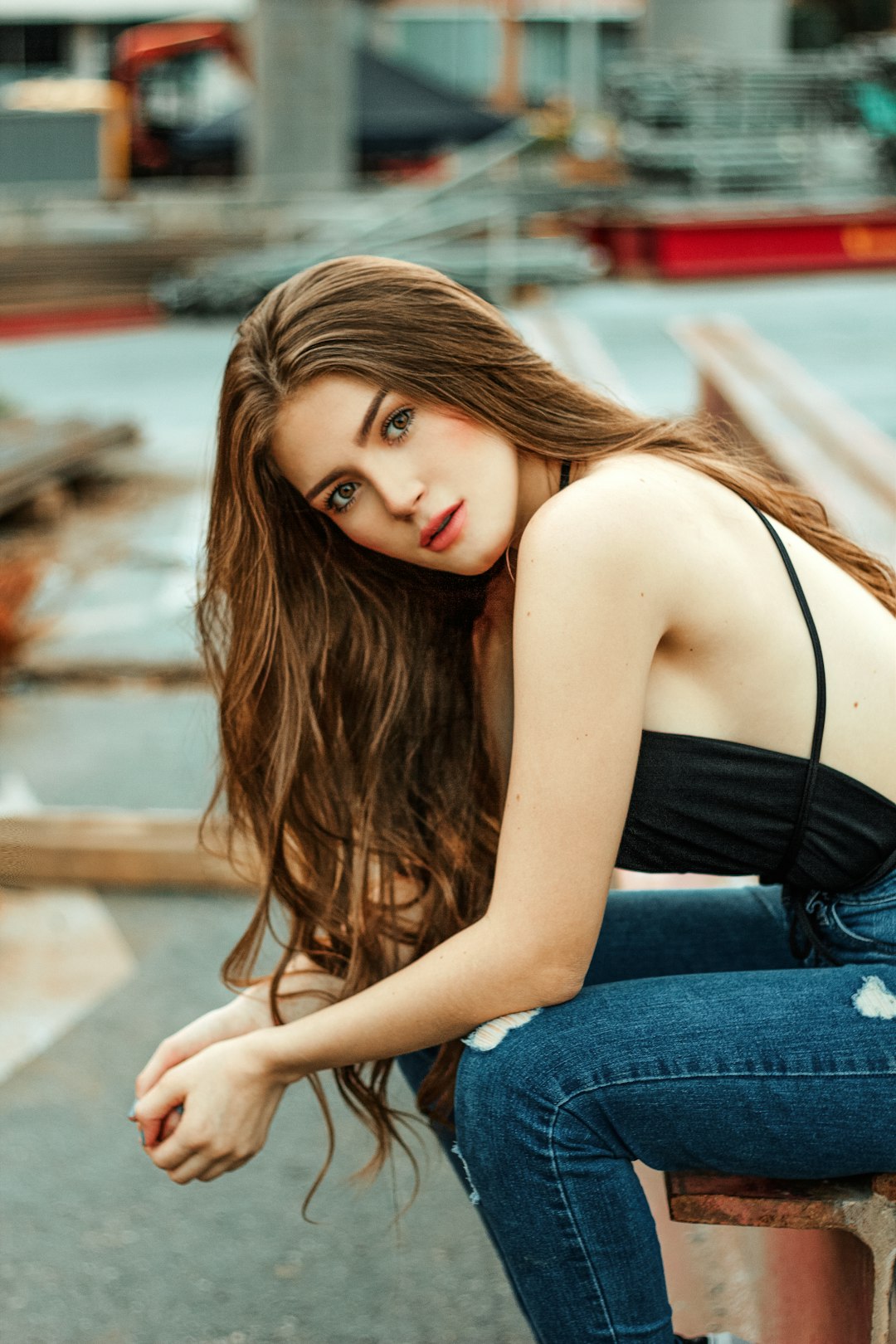 woman in black spaghetti strap top and blue denim jeans sitting on brown wooden bench during