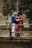man in blue jacket and woman in red dress standing on brown wooden fence during daytime
