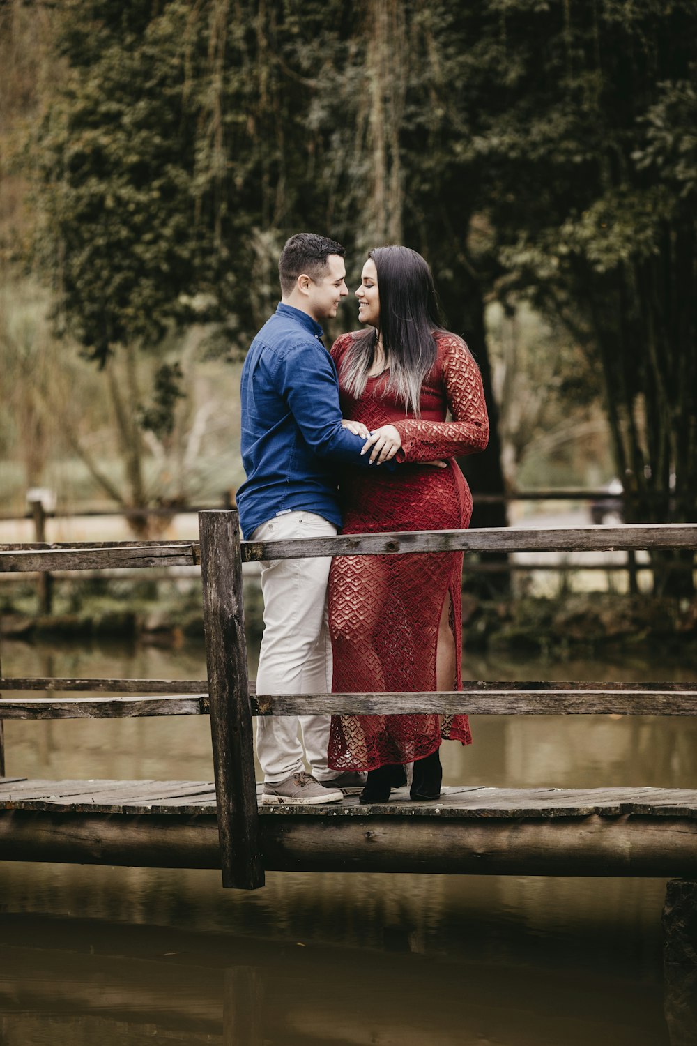 man in blue jacket and woman in red dress standing on brown wooden fence during daytime