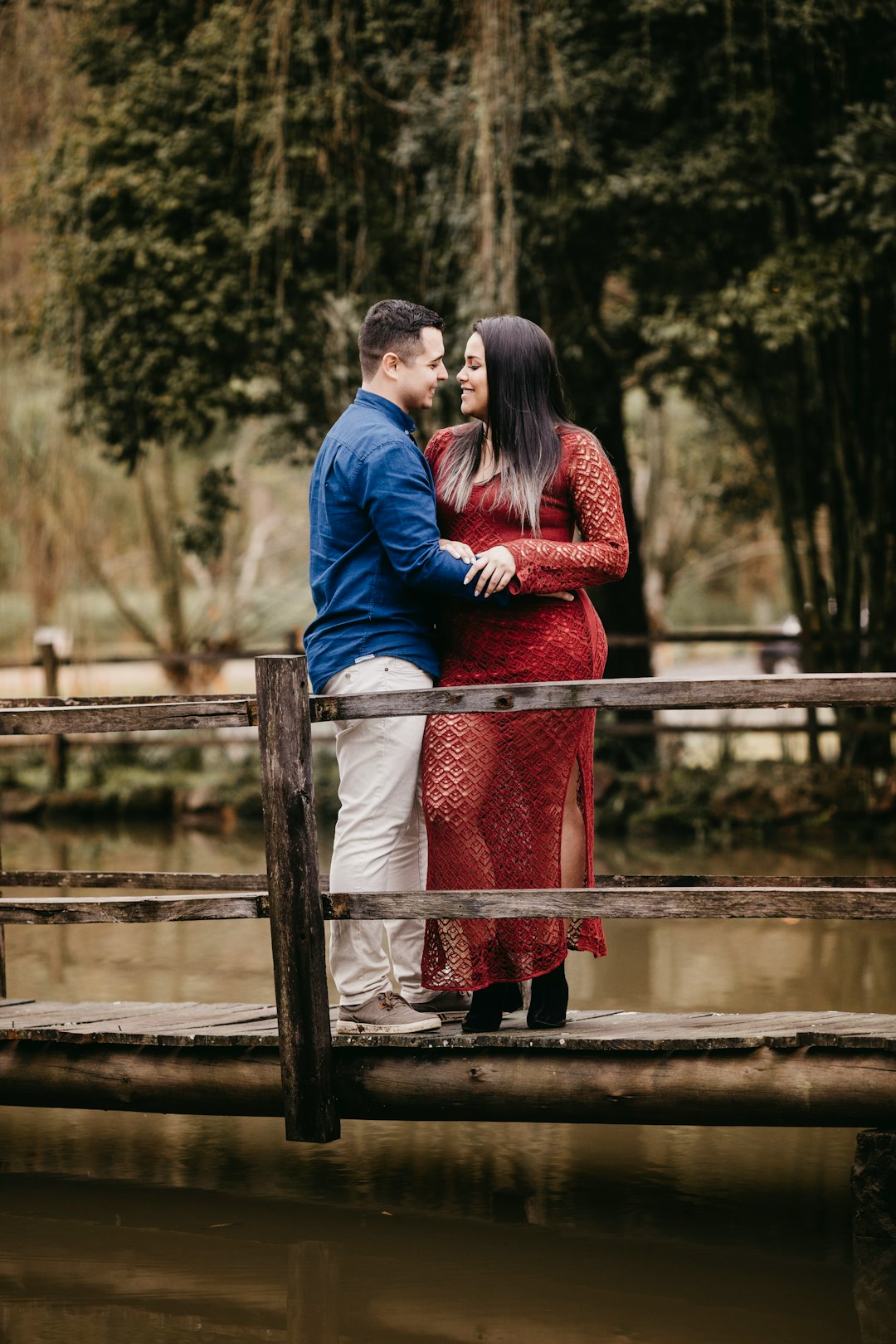 man in blue jacket and woman in red dress standing on brown wooden fence during daytime