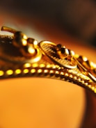 A close-up view of a gold object, possibly jewelry, featuring intricate detailing with small spherical elements and textured patterns.