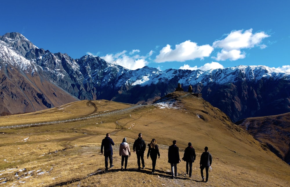 Grupo de personas de pie en el campo marrón cerca de la montaña cubierta de nieve durante el día