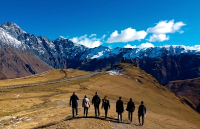 group of people standing on brown field near snow covered mountain during daytime trips teams background