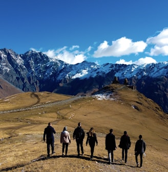 group of people standing on brown field near snow covered mountain during daytime