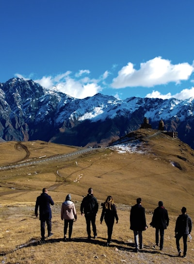 group of people standing on brown field near snow covered mountain during daytime