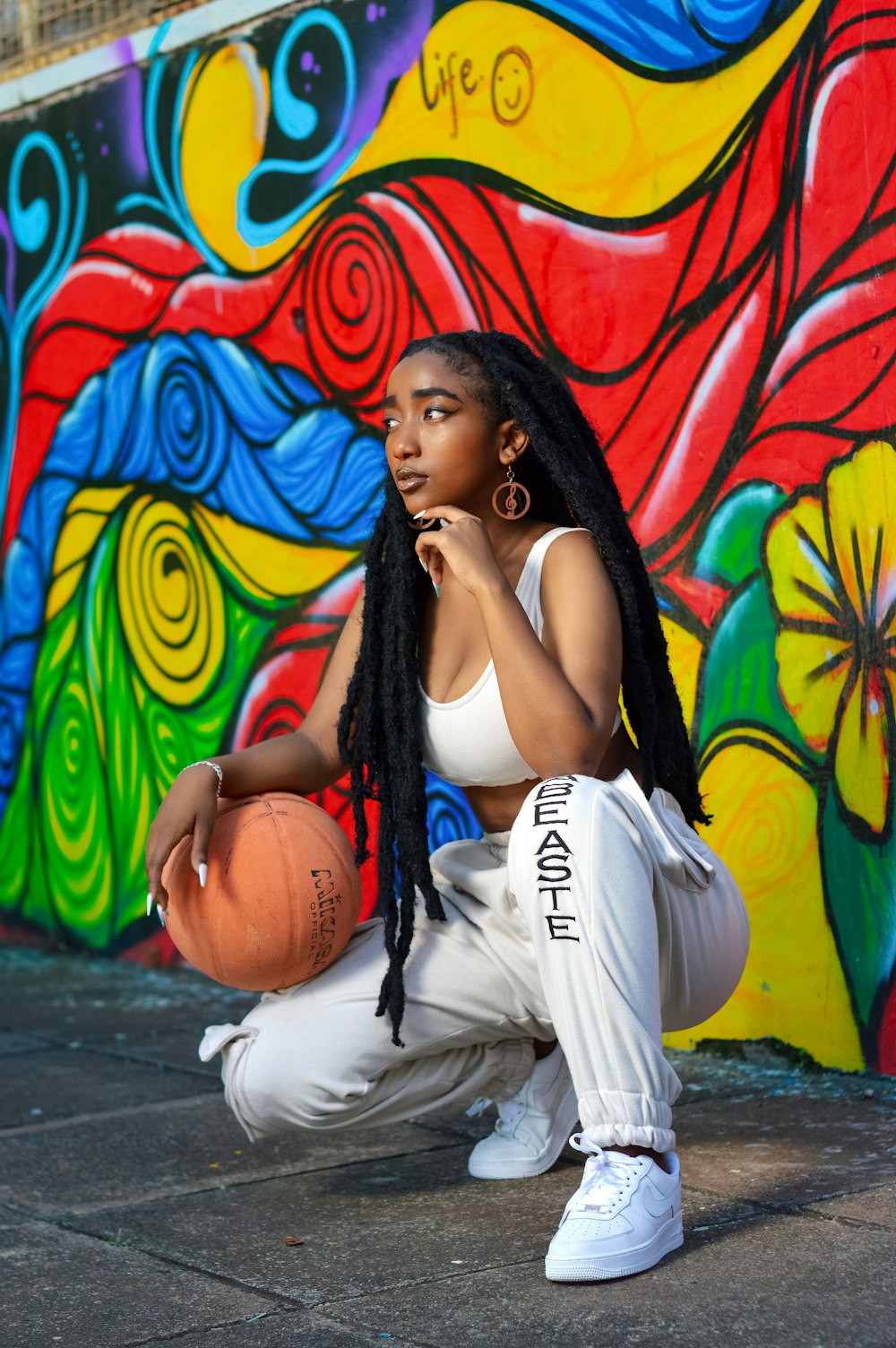 woman in black tank top and white pants sitting on floor with graffiti