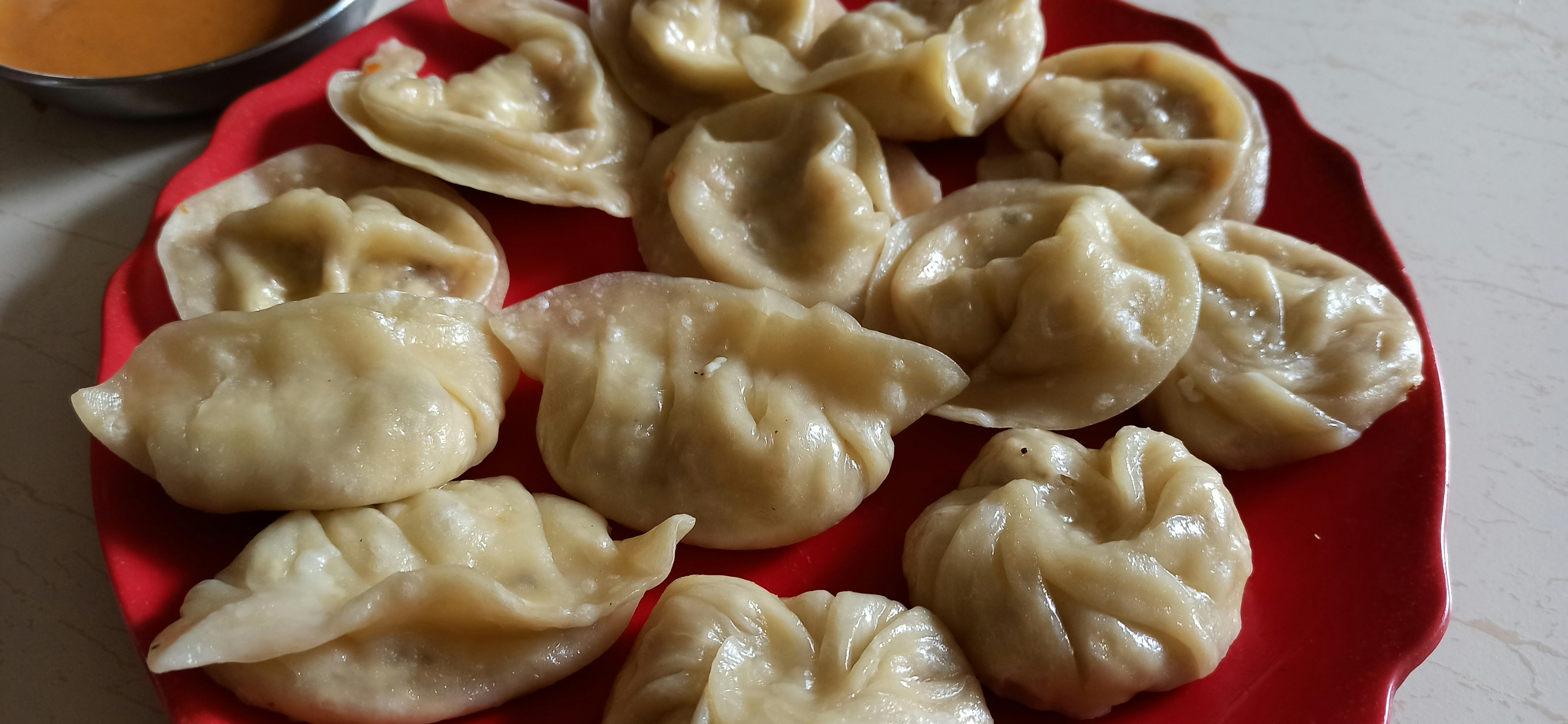 Steamed dumplings momos arranged on a plate with red chili dipping sauce