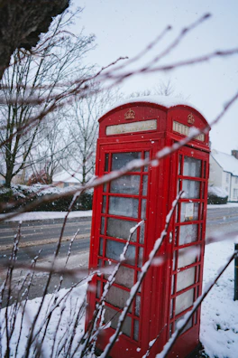 Snow-covered London street with iconic red phone booths under a soft winter sky