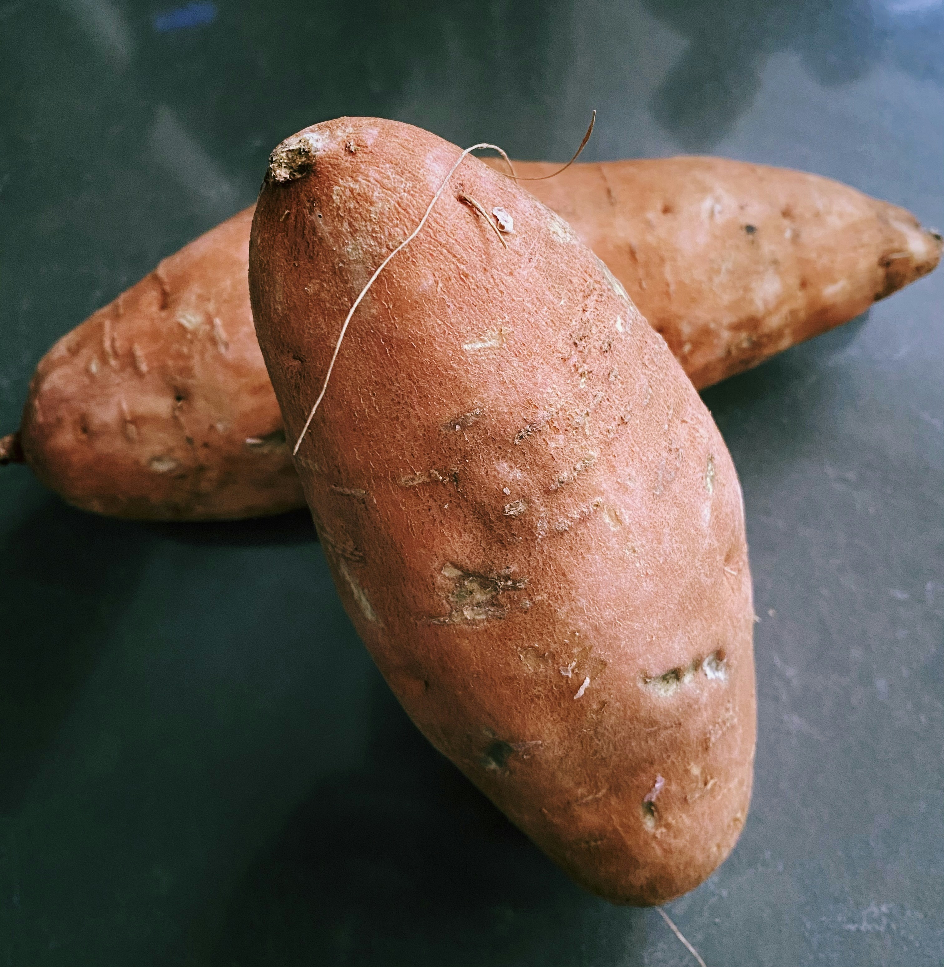 Orange sweet potatoes freshly harvested on rustic wooden surface with warm earthy tones and natural light