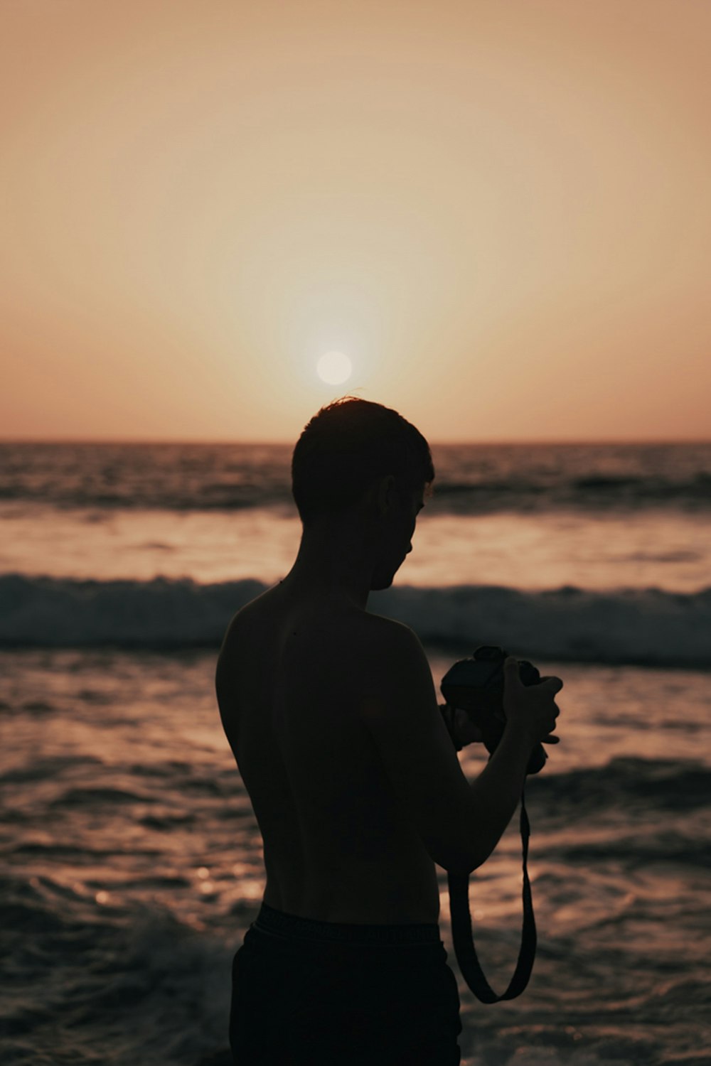 silhouette of man holding camera near body of water during sunset