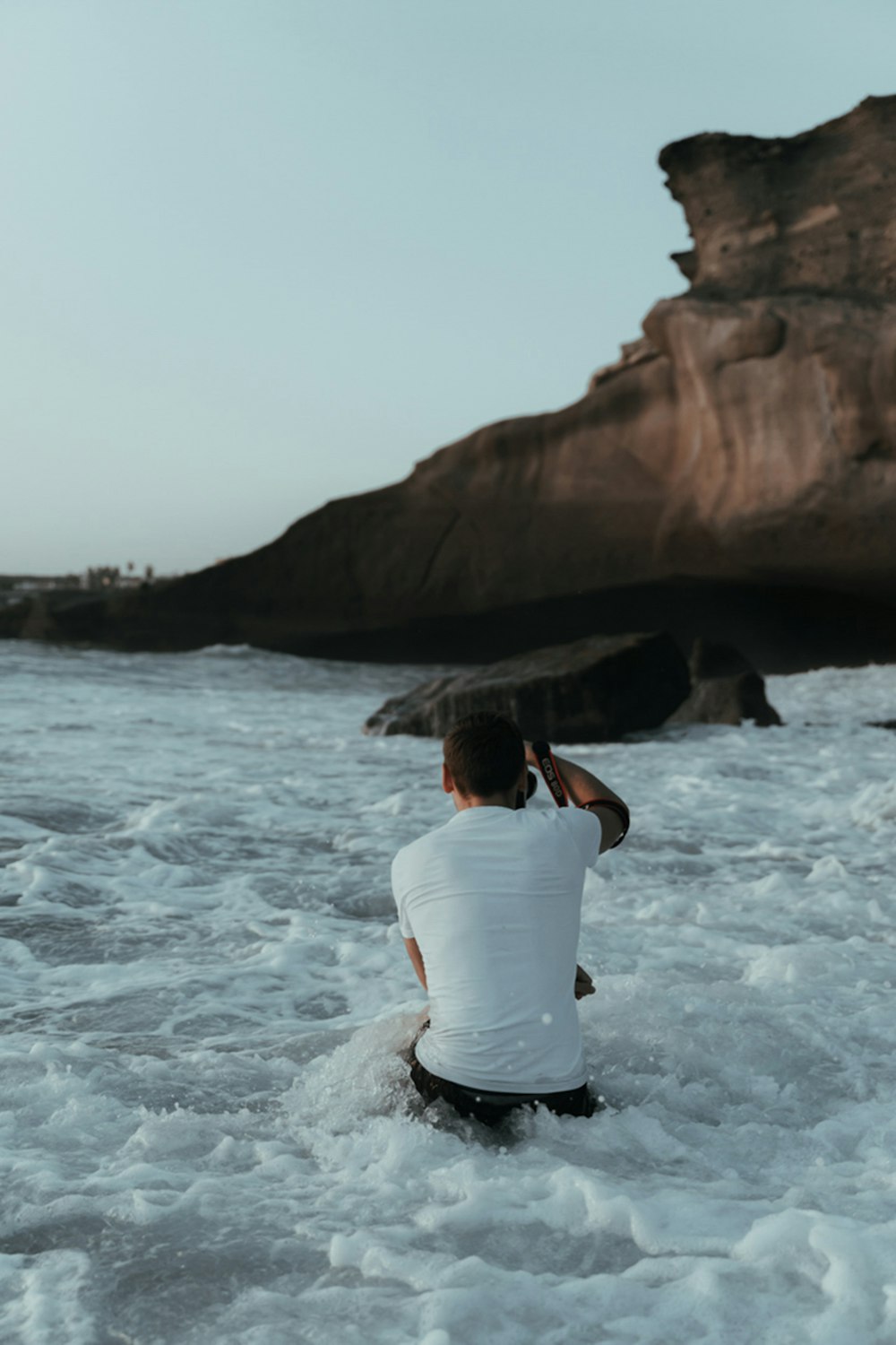 woman in white t-shirt sitting on rock formation near body of water during daytime