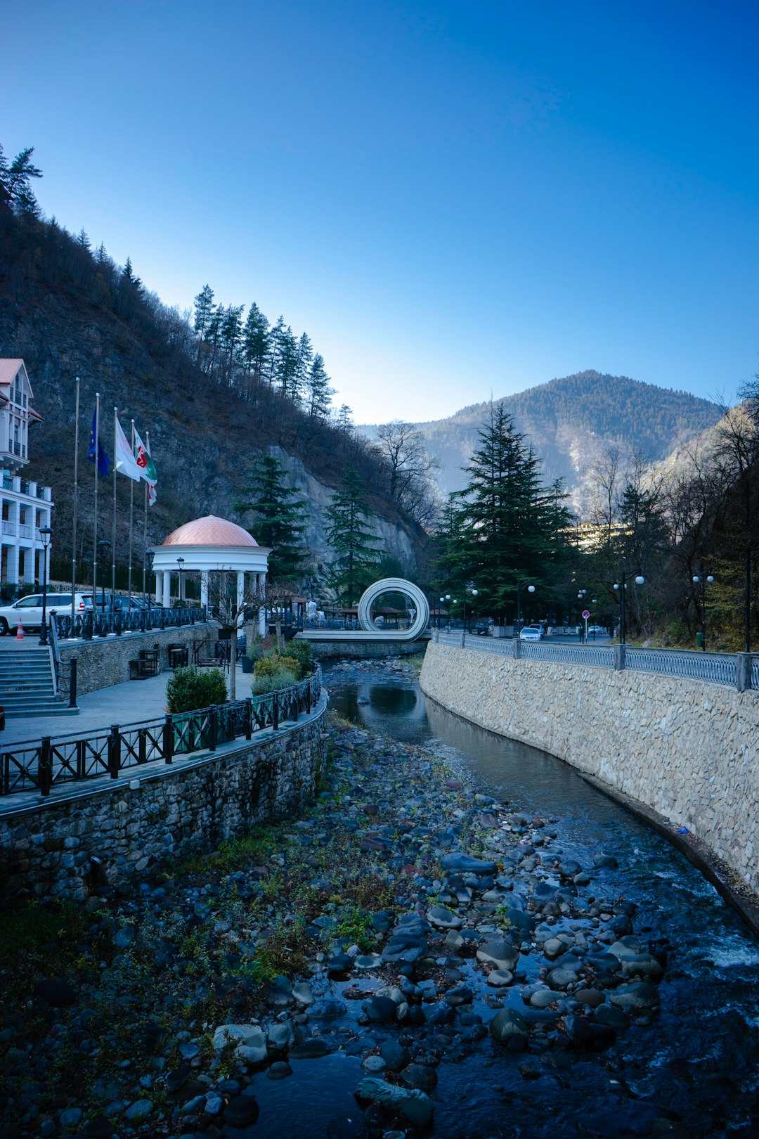 white and red concrete building near green trees and mountain under blue sky during daytime