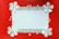 A rectangular white card bordered by a patterned black and white design is surrounded by white flowers and scattered pearls on a vibrant red background.