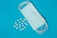 A blue medical mask lies on a blue background next to scattered yellow and white pills in various shapes and sizes.