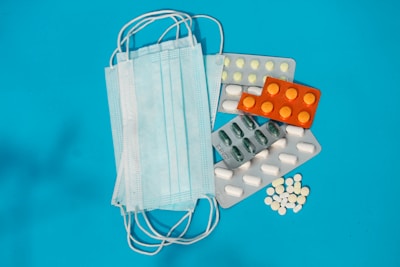 A collection of medical items, including several surgical masks and various blister packs of pills, are placed on a blue background.