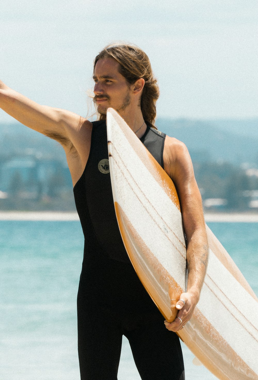 woman in black tank top holding white and brown surfboard