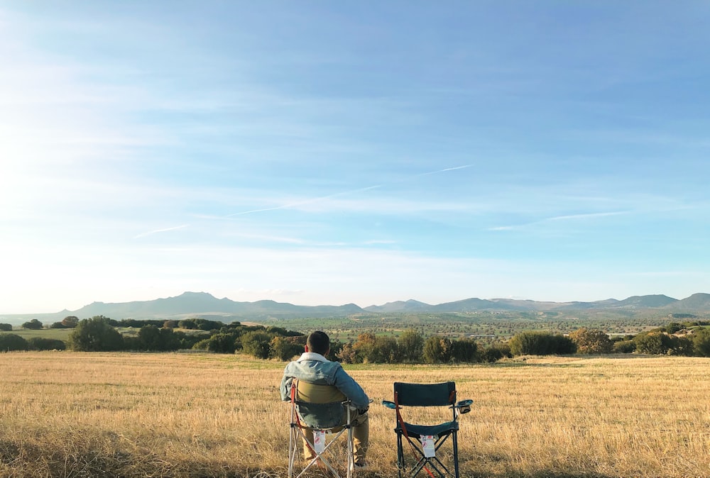 man in white shirt sitting on black chair on green grass field during daytime