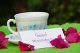 A close-up of a handwritten note with an encouraging message, resting beside a delicate teacup