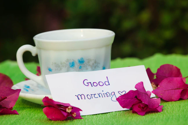 A close-up of a handwritten note with an encouraging message, resting beside a delicate teacup
