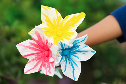 Little hands crafting colorful paper flowers beneath a shady palm tree at a lively kids event.