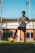 A confident young male soccer player smiling on a field, wearing a black and gold jersey.