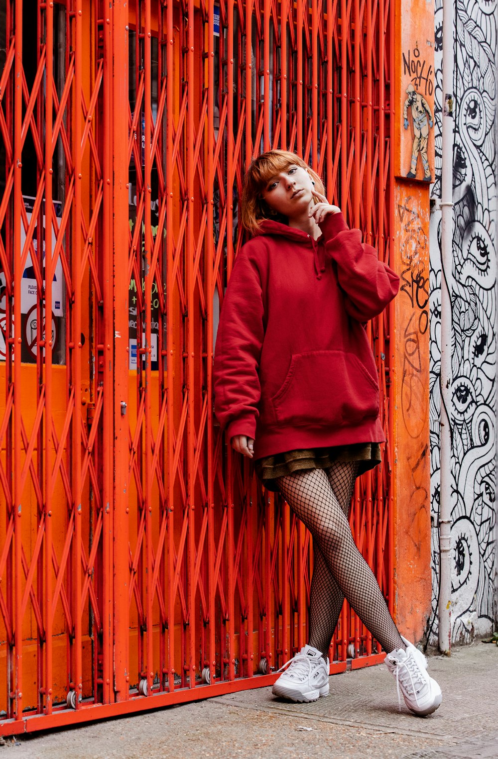 woman in red long sleeve shirt leaning on white and black floral wall