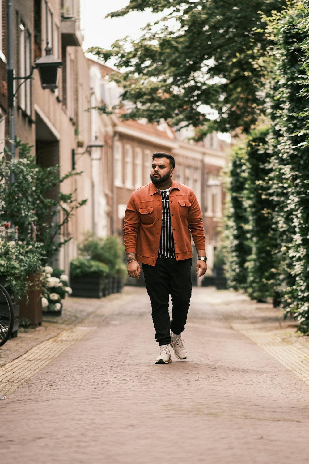 man in orange jacket and black pants standing on sidewalk during daytime