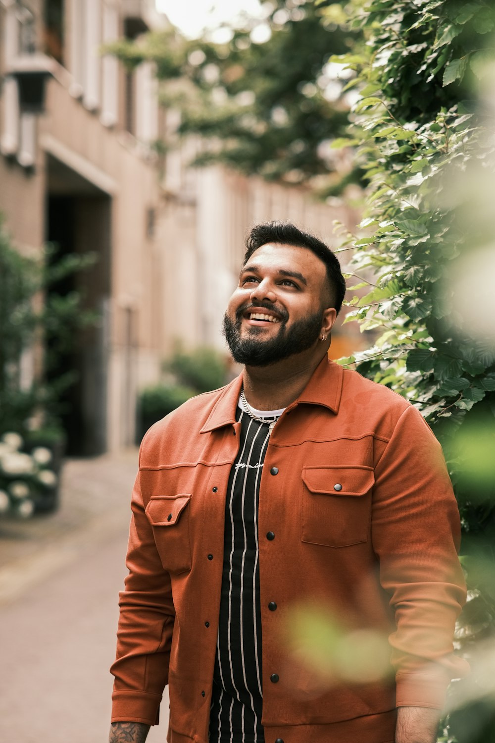 Mann in orangefarbenem Button-up-Langarmhemd steht tagsüber in der Nähe von Green Tree